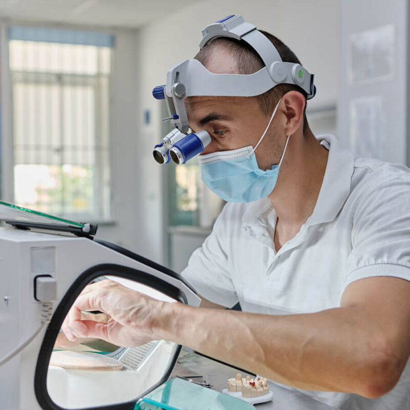 a dental technician using dental loupes and magnifying equipment to meticulously craft a prosthetic